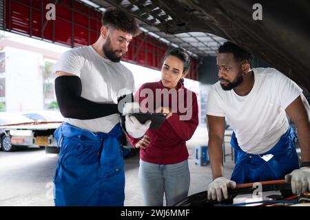 In an auto repair shop, A man professional auto mechanic briefs a female customer about the cost of car repairs and collects pay Stock Photo