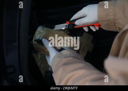 Man opening package of narcotics with stationery knife on dark background, closeup. Space for text Stock Photo