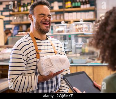 Woman Using Digital Tablet Working In Food Shop Training Man With Down Syndrome Holding Bread Stock Photo