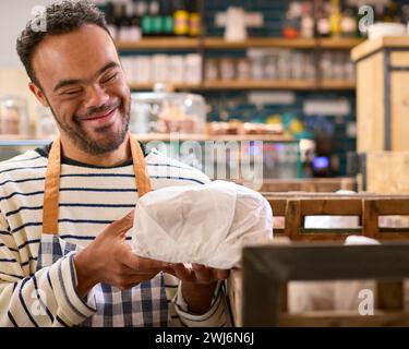 Smiling Man With Down Syndrome Stocking Shelf With Bread In Food Shop Stock Photo