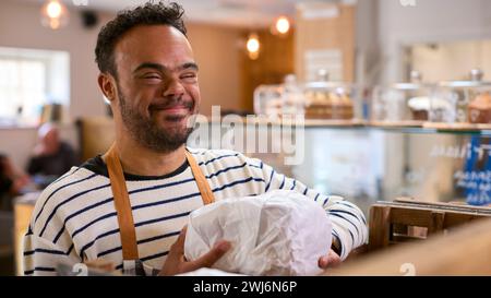 Smiling Man With Down Syndrome Stocking Shelf With Bread In Food Shop Stock Photo