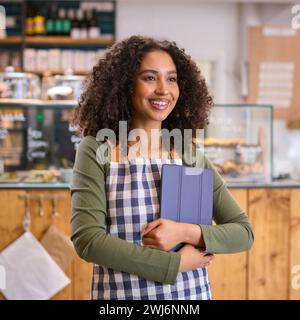 Smiling Young Woman Wearing Apron Working In Food Shop Using Digital Tablet Stock Photo