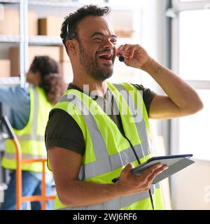 Man With Down Syndrome Working In Warehouse Wearing Headset Using Digital Tablet Stock Photo