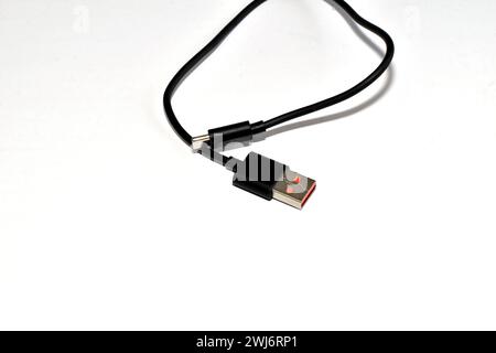 A short USB cable of a black body lies randomly on a white background. Stock Photo