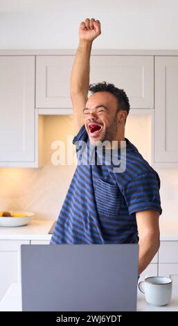 Man With Down Syndrome At Home Using Laptop Celebrating Good News Stock Photo