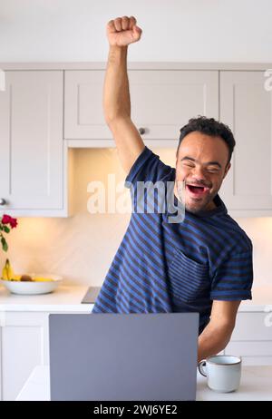 Man With Down Syndrome At Home Using Laptop Celebrating Good News Stock Photo