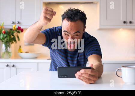 Man With Down Syndrome At Home Celebrating Streaming Sport To Mobile Phone Stock Photo