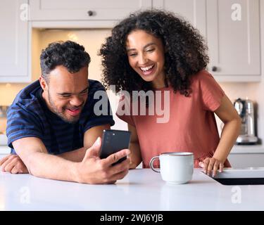 Couple At Home With Man With Down Syndrome Looking At Mobile Phone Together Stock Photo