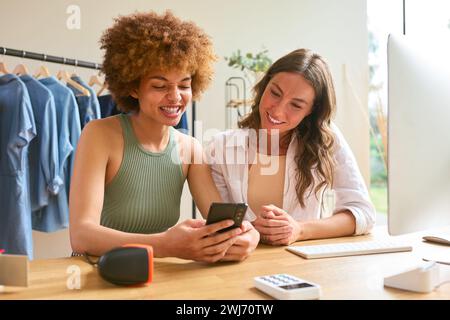 Two Women Friends Running Online Fashion Business From Home Checking Social Media On Mobile Phone Stock Photo