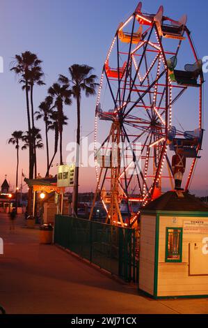 A small Ferris wheel is illuminated agains the dusk sky at the Balboa Fun Zone, an amusement park in Newport Beach California Stock Photo