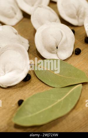 Traditional classic meat dumplings, uncooked, still life on a wooden board with black pepper corns and green bay leaves Stock Photo