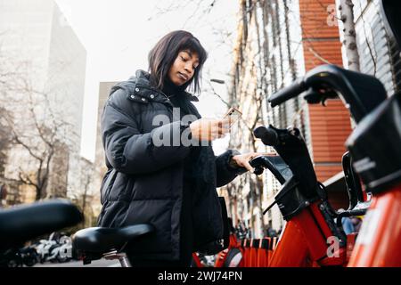 Young beautiful woman taking a public bicycle on the street. Woman using a heathy and clean transport in a city. Stock Photo