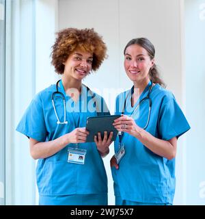 Portrait Of Two Female Doctors Wearing Scrubs With Digital Tablet In Hospital Stock Photo