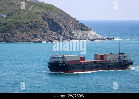 Small container cargo ship HUI HAI LONG 388 loaded with containers entering Tathong channel in Hong-Kong, Tung Lung Chau island rocky cliffs & caves Stock Photo