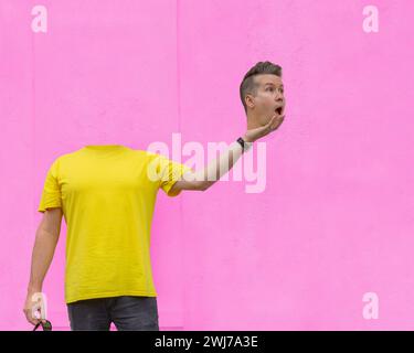 A man who has lost his head, with a surprised expression, and is holding it in front of a pink wall Stock Photo