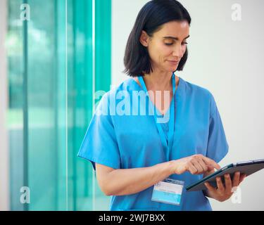 Mature Female Doctor Wearing Scrubs Using Digital Tablet In Hospital Stock Photo