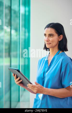 Mature Female Doctor Wearing Scrubs Using Digital Tablet In Hospital Stock Photo