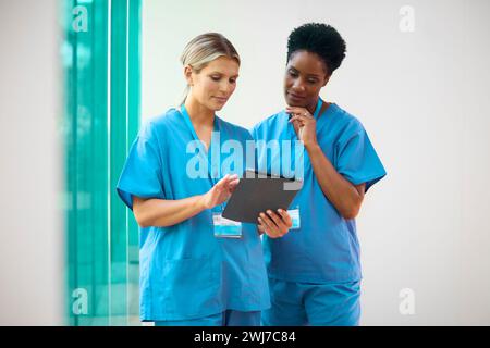 Two Mature Female Doctors Wearing Scrubs With Digital Tablet Discussing Patient Notes In Hospital Stock Photo