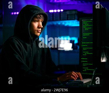 Low Key Lighting Shot Of Male Computer Hacker Sitting In Front Of Screens Breaching Cyber Security Stock Photo
