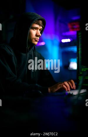 Low Key Lighting Shot Of Male Computer Hacker Sitting In Front Of Screens Breaching Cyber Security Stock Photo