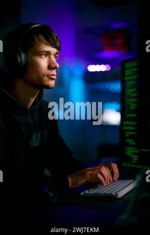 Low Key Lighting Shot Of Male Computer Hacker Sitting In Front Of Screens Breaching Cyber Security Stock Photo
