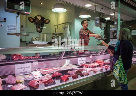 Butcher weighing meat for a customer in the old Abaceria Central Market, Barcelona Stock Photo