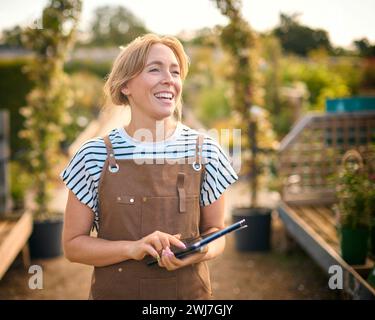 Woman Working Outdoors In Garden Centre Using Digital Tablet Stock Photo