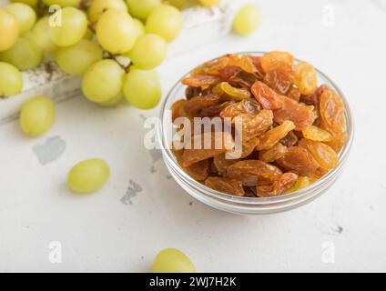 Sweet dried green raisins in glass bowl with ripe grapes in wooden box on light kitchen background.Macro Stock Photo