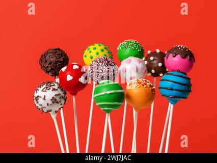 Homemade cake pops with various icings colors, minimalist on a red background. Stock Photo