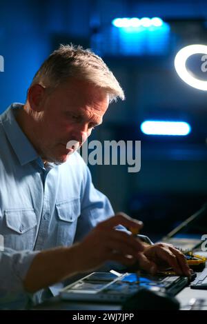 Mature Male Electronics Expert Repairing Laptop In Workshop With Low Key Lighting Stock Photo