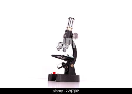 an old microscope stands isolated on a white background on a white surface with real shadows Stock Photo