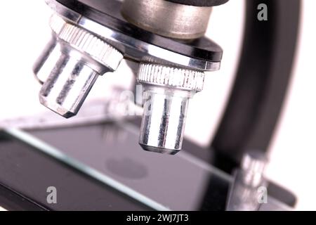 an old microscope stands isolated on a white background on a white surface with real shadows Stock Photo