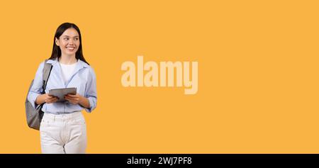 Smiling lady student using digital tablet with standing with backpack, looking at free space Stock Photo