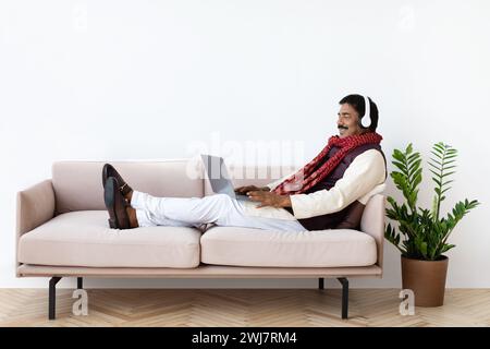 Relaxed mature indian man using laptop and headset Stock Photo