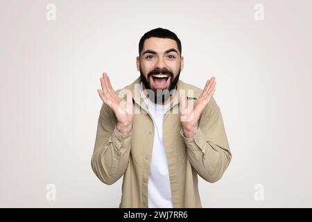 Glad shocked handsome young middle eastern guy with beard in casual look at camera with hands Stock Photo