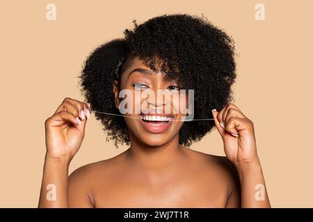 Joyful black woman with curly hair flossing her teeth Stock Photo