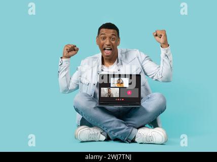 An ecstatic young man in a denim jacket and jeans sits cross-legged Stock Photo