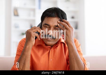 Upset mature indian man have phone conversation at home Stock Photo