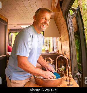 Senior Man Enjoying Camping In Countryside Relaxing Inside RV And Doing Chores Stock Photo