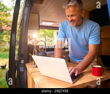 Senior Man On Camping Trip In Countryside Working Inside RV Using Laptop Stock Photo