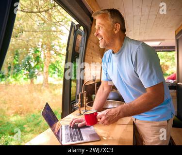 Senior Man On Camping Trip In Countryside Working Inside RV Using Laptop Stock Photo