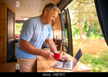 Senior Man On Camping Trip In Countryside Working Inside RV Using Laptop Stock Photo