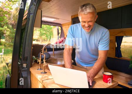 Senior Man On Camping Trip In Countryside Working Inside RV Using Laptop Stock Photo