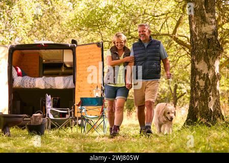 Senior Couple Camping In Countryside With RV Taking Labrador Dog For A Walk Stock Photo