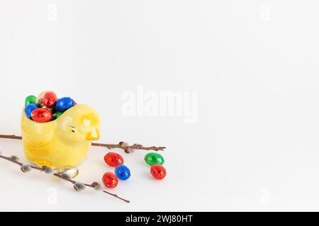 Colourful chocolate eggs in yellow ceramic chick next to palm kitten, white background, copy room Stock Photo