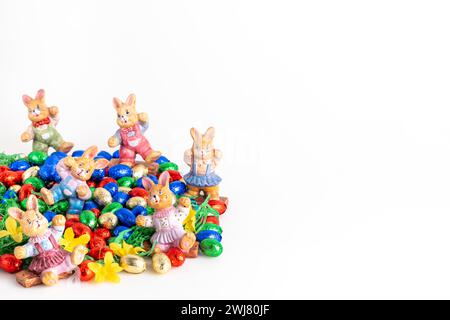 Several Easter bunny figures surrounded by colourful chocolate eggs on artificial grass, white background Stock Photo