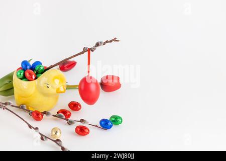 Red Easter egg hanging on a willow branch with tulips and chocolate eggs, white background, copy space Stock Photo