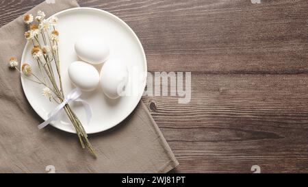 Easter table setting with white eggs and dried flowers on wooden background. Stock Photo