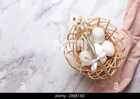 Easter eggs in a basket on a white marble background with a pink napkin and copy space. Stock Photo