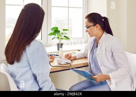 Female doctor measuring blood pressure of pregnant young woman in medical clinic. Stock Photo